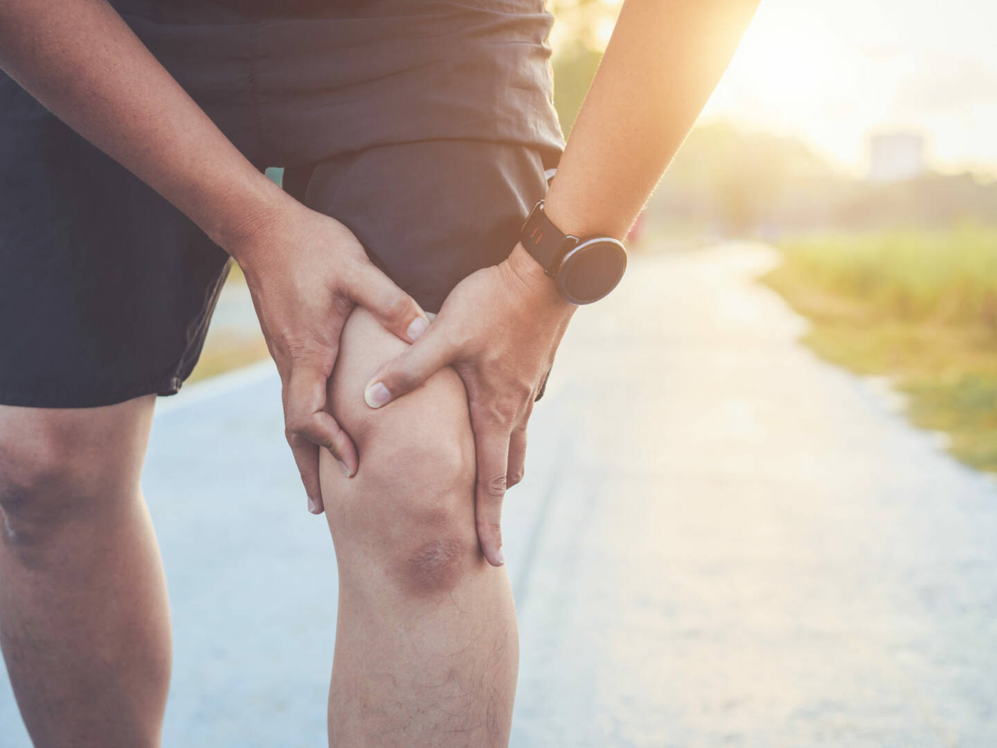 Runner stopping on a path to hold an aching knee