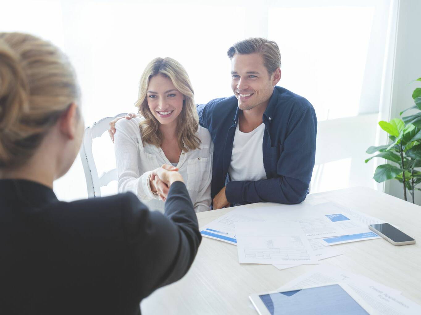 Couple shaking hands with an escrow officer across a table of documents
