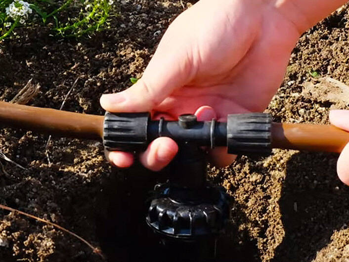Hands installing an irrigation valve fitting in a trench