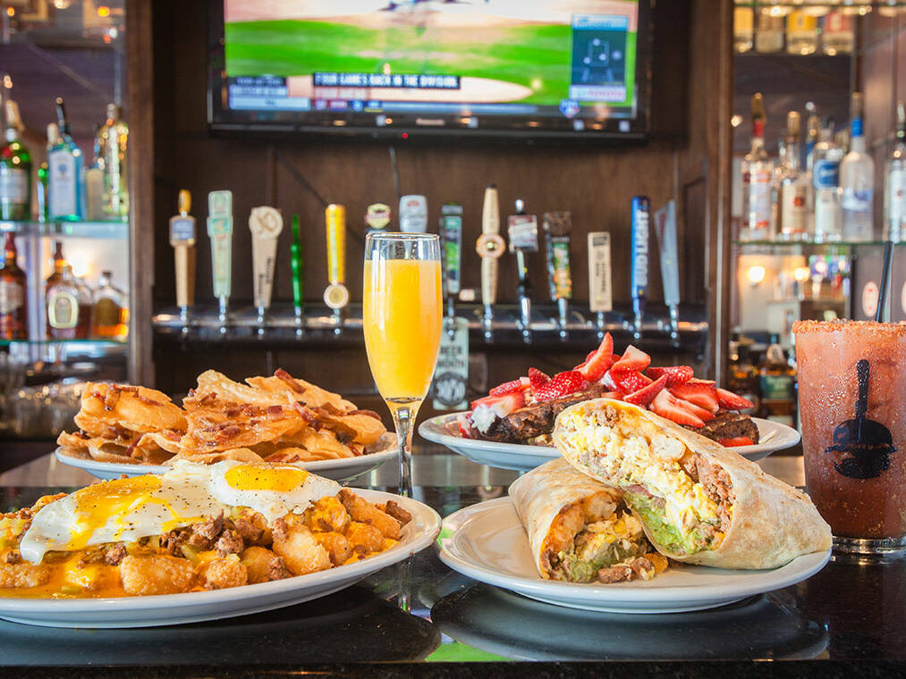 Brunch spread of waffles, breakfast burrito, tater tots, and cocktails on a bar top
