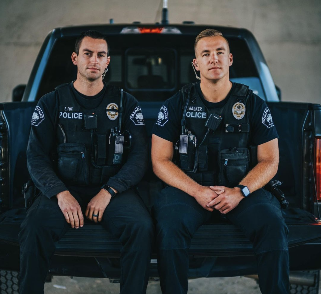 Two Corona police officers seated on the tailgate of a department truck