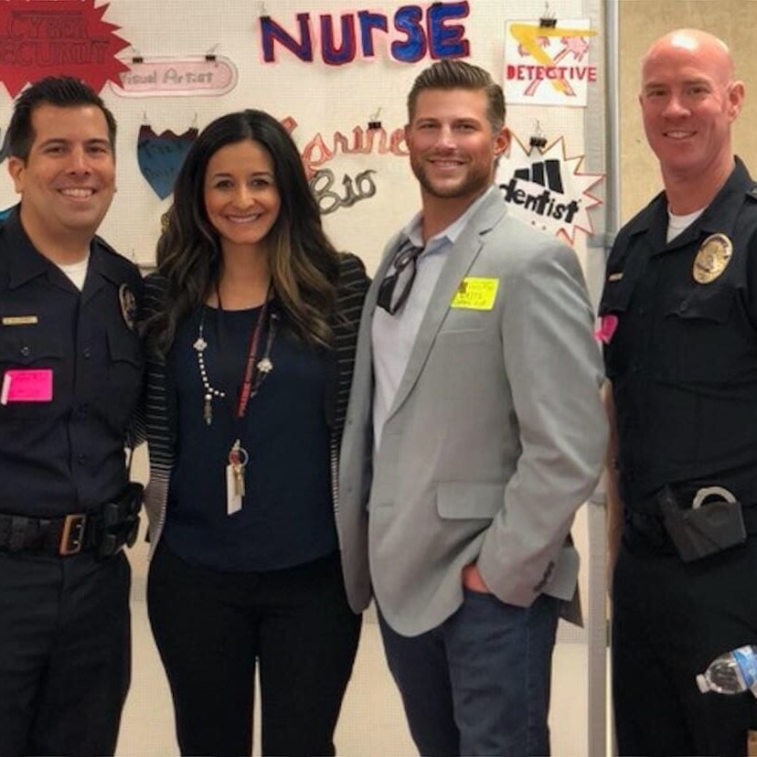 Four adults standing in front of a wall of career signs reading nurse, detective, visual artist, marine biologist, and dentist at a community career event