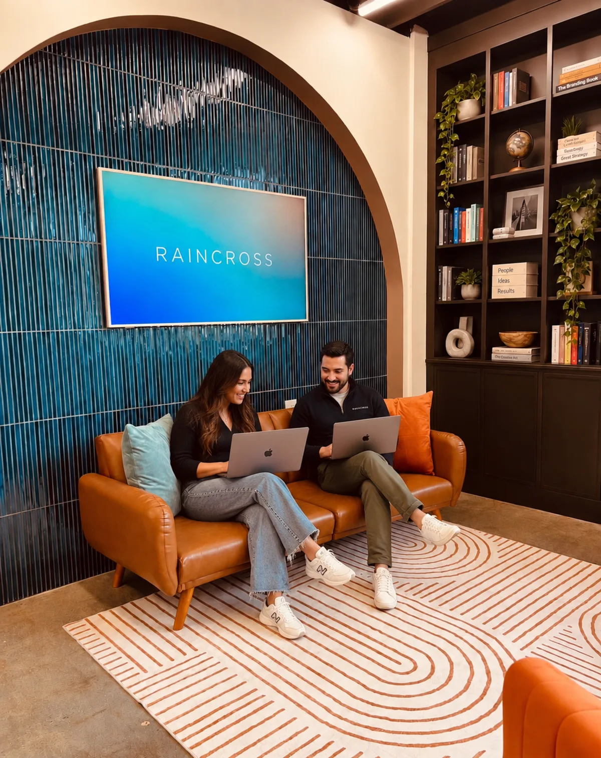 Two Raincross team members working on laptops in the studio lounge beneath the Raincross sign