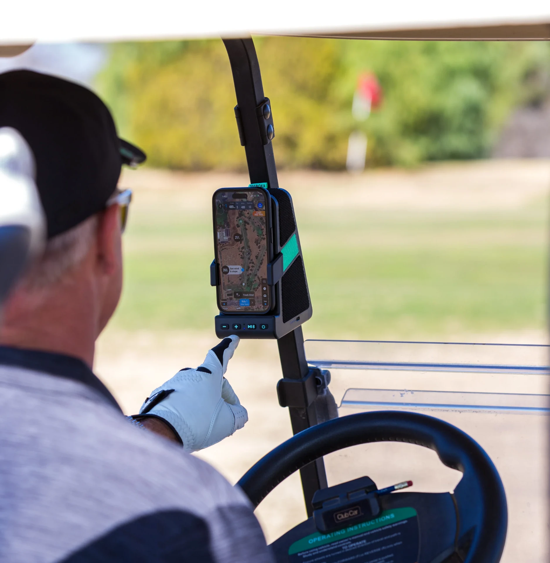 Golfer in a cart reaching for the TeeBoxx mounted on the cart frame with a course app on screen