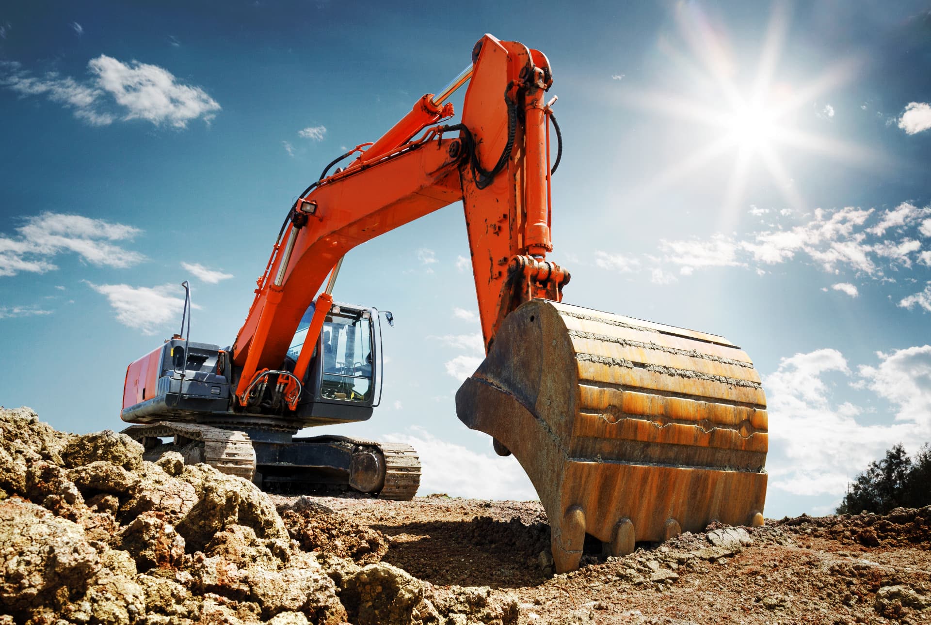 Excavator working a graded site under bright sun during an environmental remediation project