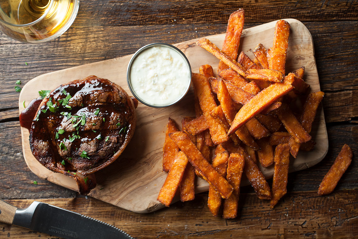 Grilled steak with sweet potato fries and dipping sauce on a wooden board