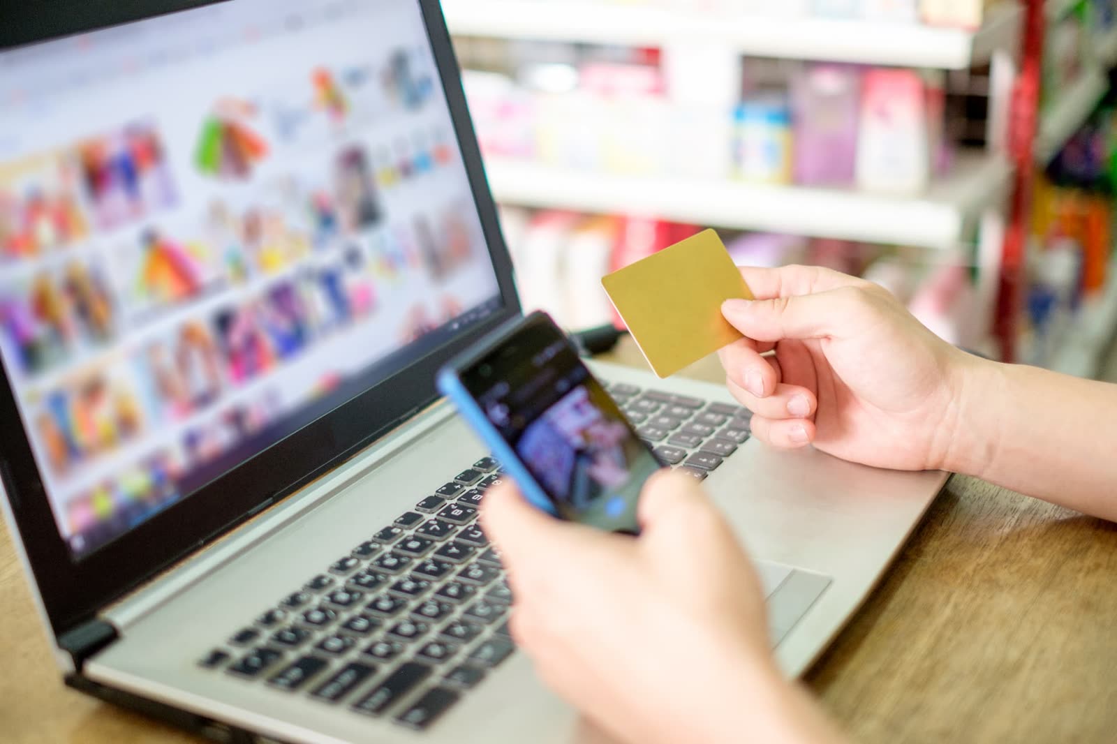 A shopper holding a credit card and phone while browsing an online store on a laptop