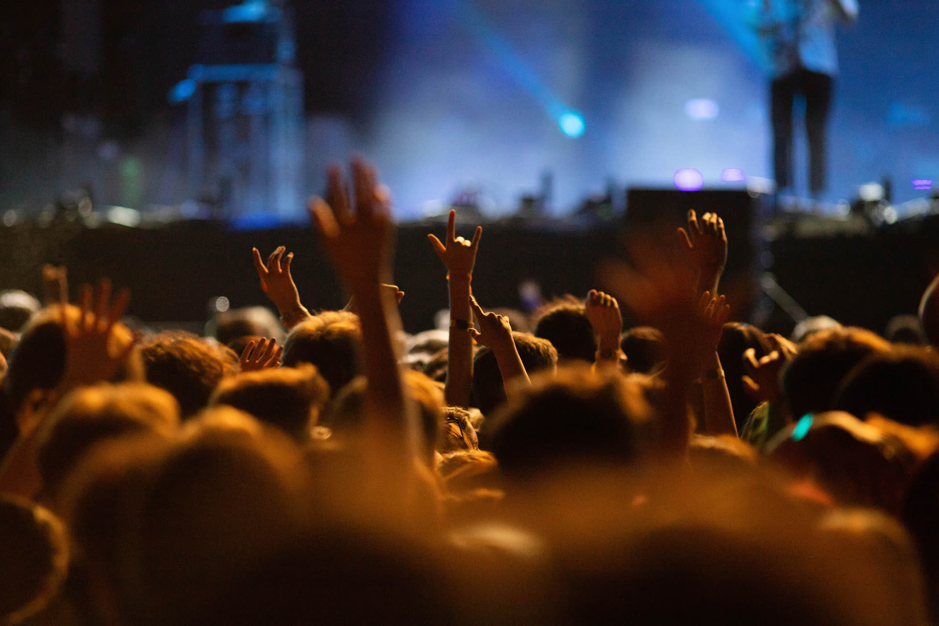 Concert crowd with hands raised in front of a stage lit in blue