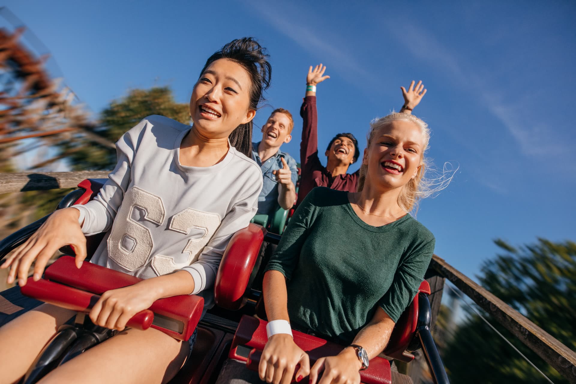 Friends laughing with hands raised on a roller coaster at a sunny amusement park